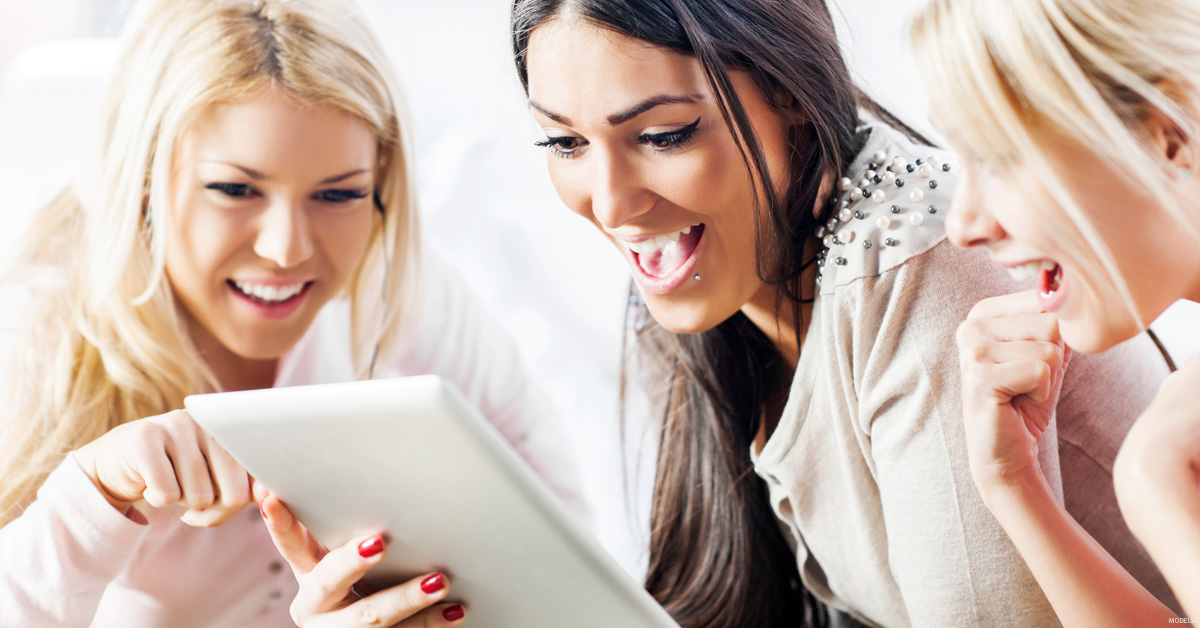 3 young woman smiling as they look at computer tablet