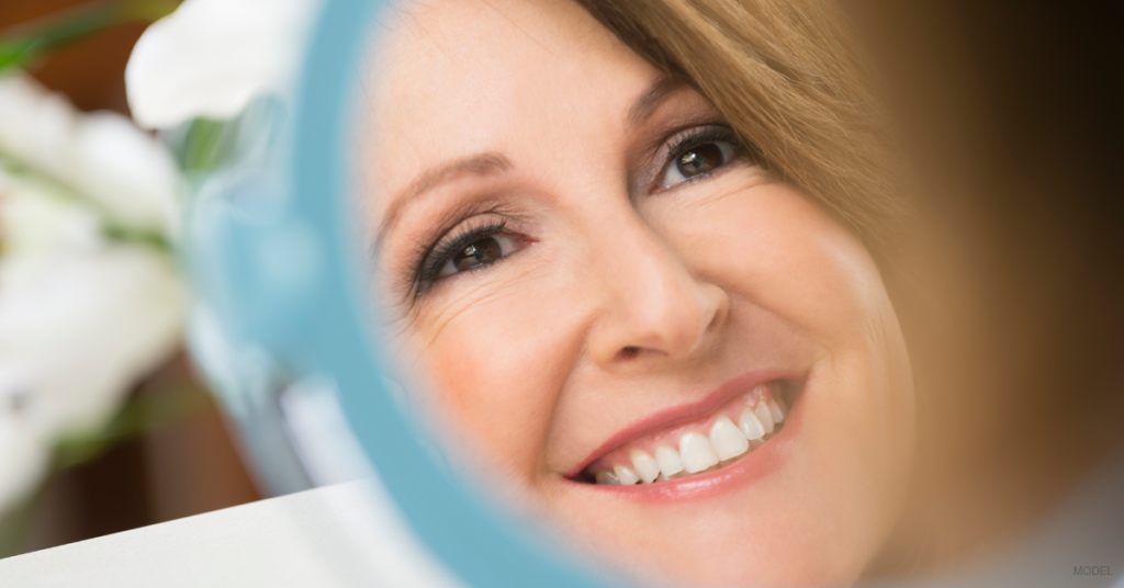 A woman looks in the mirror and contemplates the benefits of getting a facelift.