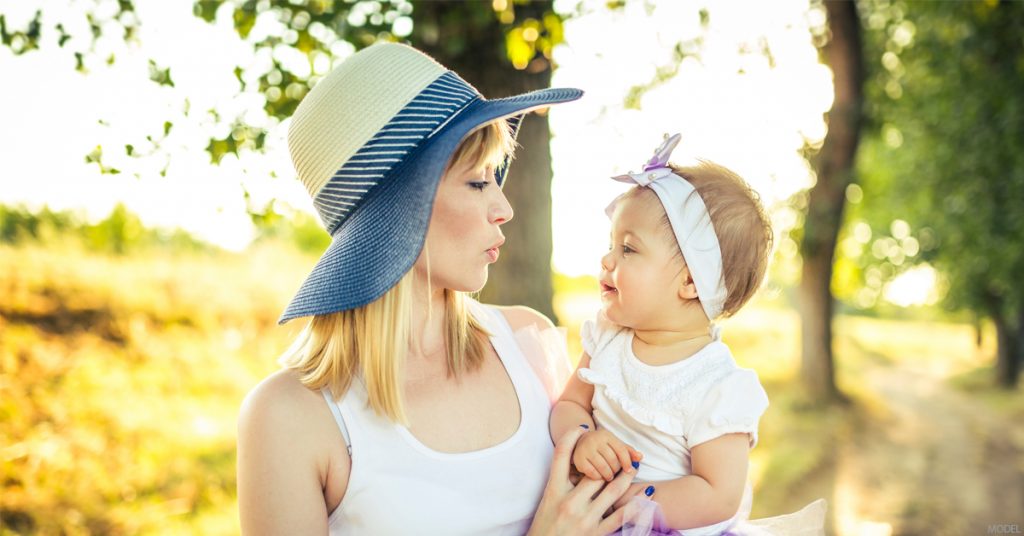 A new mother considering a mommy makeover holds her baby in a park