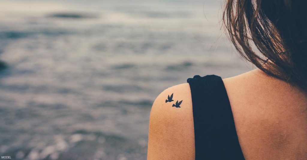 Woman with tattoos (model) looking out over the ocean.