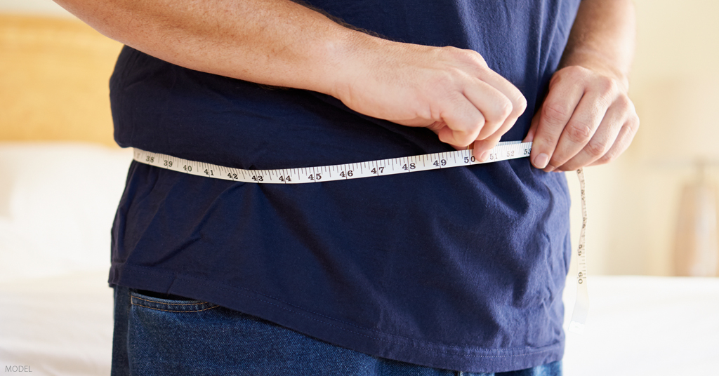 A man measures his waistline after receiving a body lift.