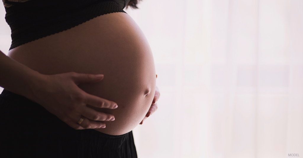 A woman holds her stomach as she considers the pros and cons of a c tuck.