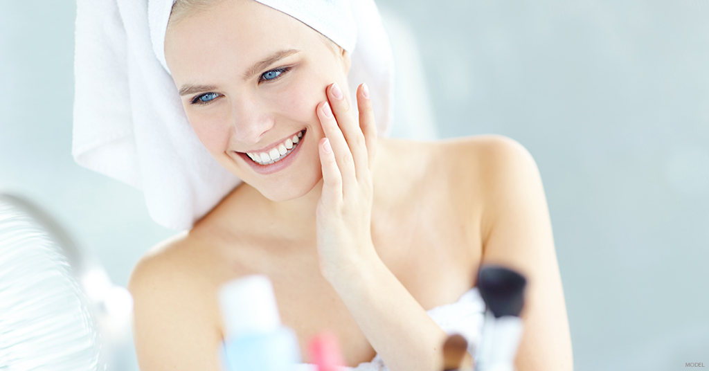 A woman looks happy with her skin while doing her skin care routine.